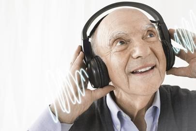 En leende äldre man som lyssnar på musik i svarta hörlurar.